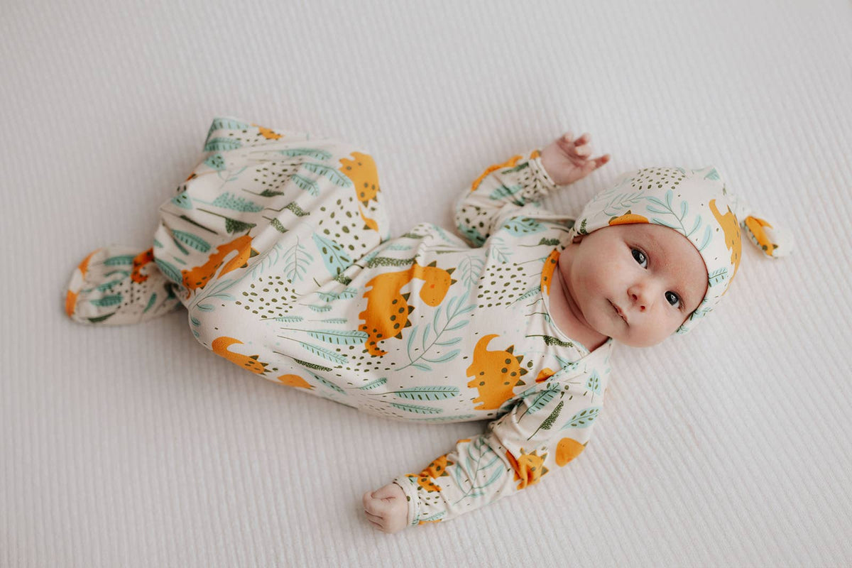 Three Little Tots - Dinosaur Animal Print Zoo Knotted Gown — baby gown with dinosaur print shown flat beside baby