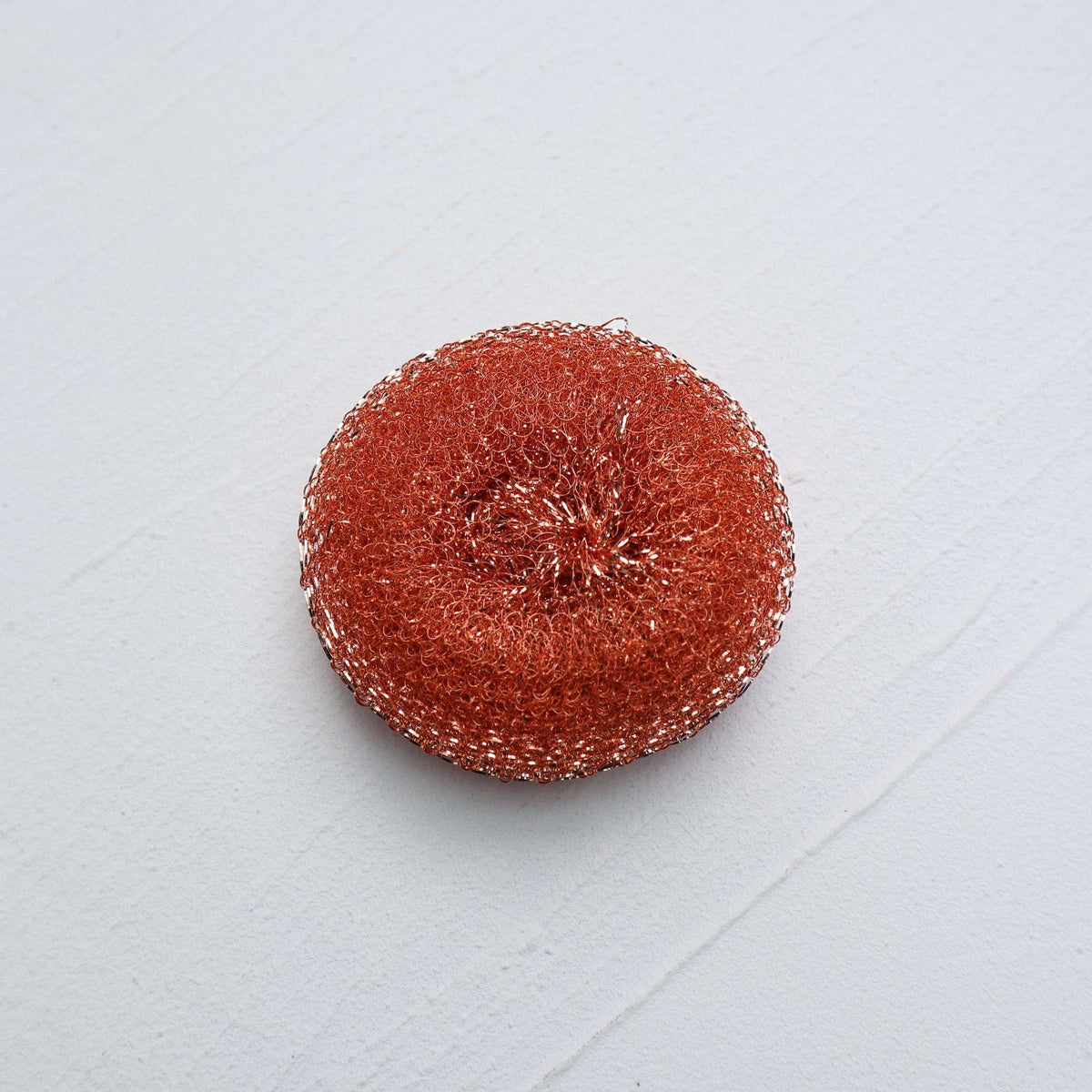 Plantish recycled-copper pop-up dish scrubby, round copper scrubbing pad on white tile in overhead view