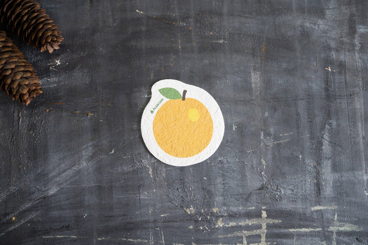Plantish plastic-free compostable orange cellulose sponge, orange-shaped sponge laid on dark stone background