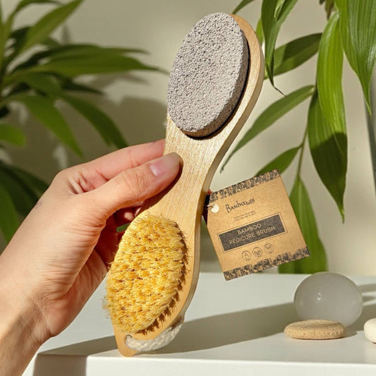 Bamboo Switch Bamboo Exfoliating Foot Pedicure Tool - hand holding yellow foot file with wooden handle near plants