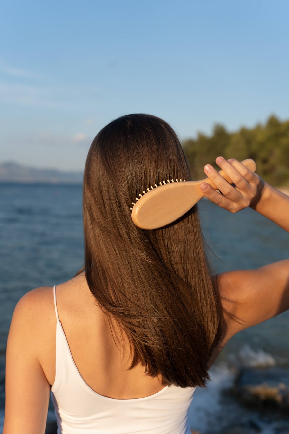 Croll & Denecke vegan birch wood paddle hairbrush, woman brushing long hair by the sea