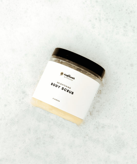 Sunflower Motherhood brightening body scrub — open body scrub jar on pale stone background