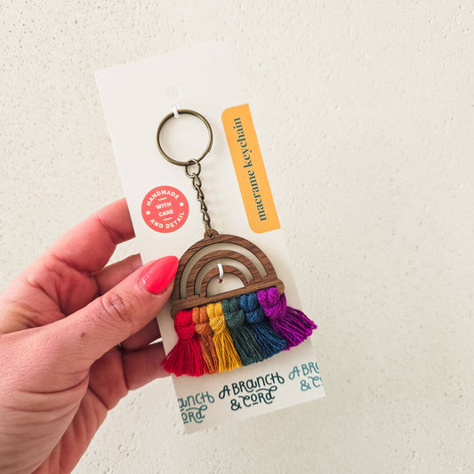 A Branch & Cord cotton macrame rainbow tassel keychain, hand holding colorful macrame rainbow on hang card
