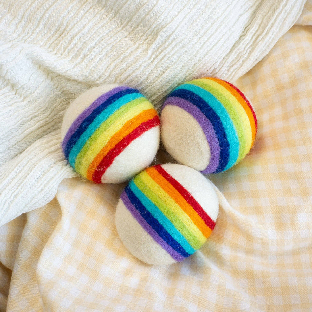 Friendsheep compostable rainbow wool dryer balls set of three: three rainbow-striped dryer balls arranged on pale fabric