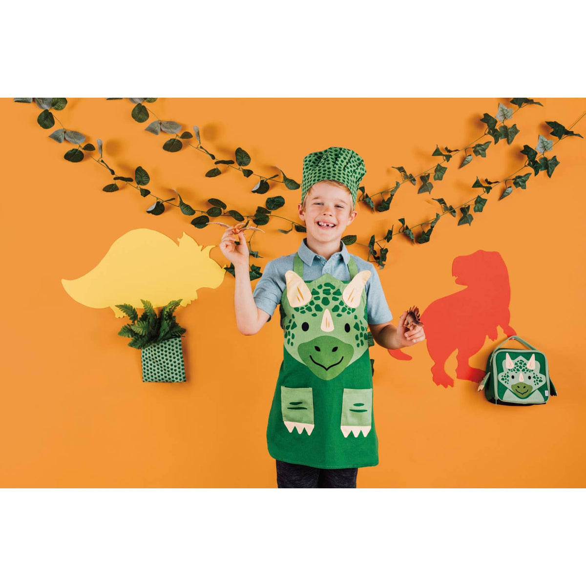Danica Jubilee reusable dinosaur print snack bags, child with dinosaur themed snack bags on orange backdrop