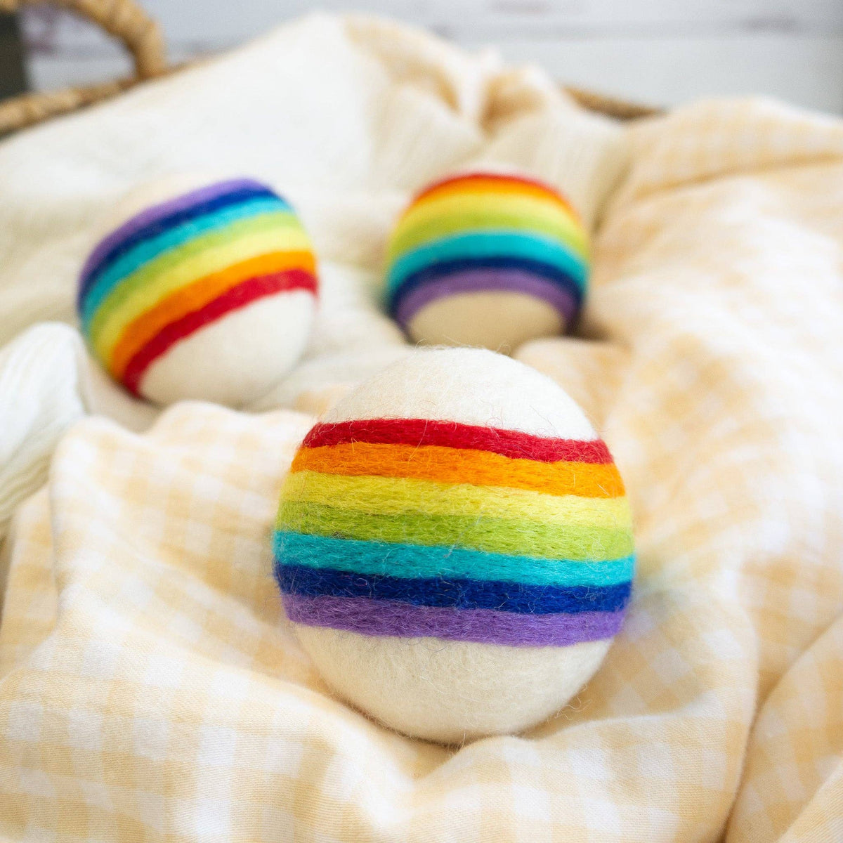 Friendsheep compostable rainbow wool dryer balls set of three: three colorful striped wool laundry balls beside woven basket